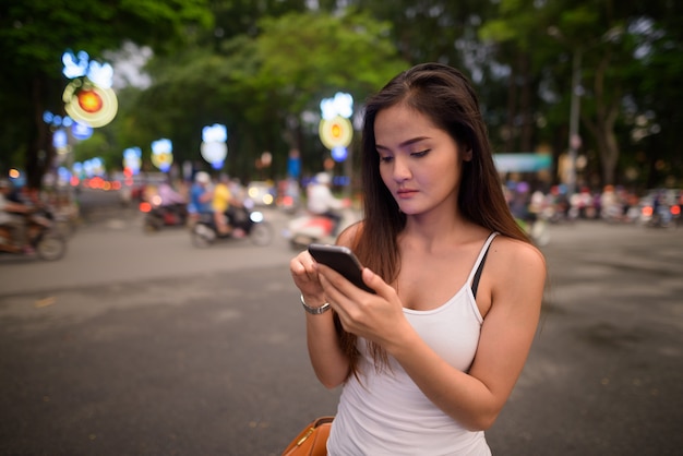 Young beautiful Asian tourist woman using mobile phone outdoors