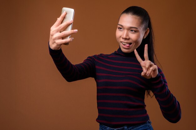 Young beautiful Asian transgender woman against brown background