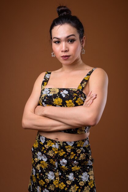 Young beautiful Asian transgender woman against brown background