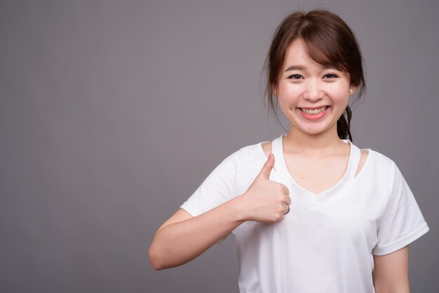 Young beautiful Asian woman against gray wall