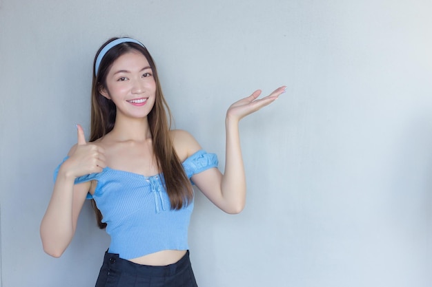 Young beautiful Asian woman in blue shirt is acting thumb up as good symbol and another hand shows