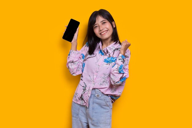 young beautiful asian woman demonstrating mobile cell phone isolated on yellow background