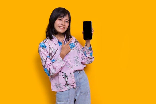 Young beautiful asian woman demonstrating mobile cell phone isolated on yellow background