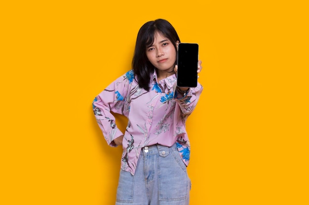 Young beautiful asian woman demonstrating mobile cell phone isolated on yellow background