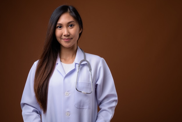 Young beautiful Asian woman doctor against brown background