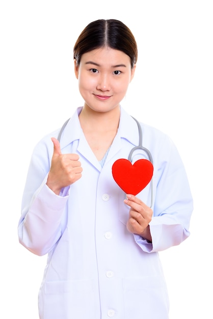 Young beautiful Asian woman doctor holding red heart and giving thumb up