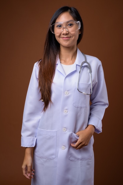 Young beautiful Asian woman doctor wearing protective glasses ag