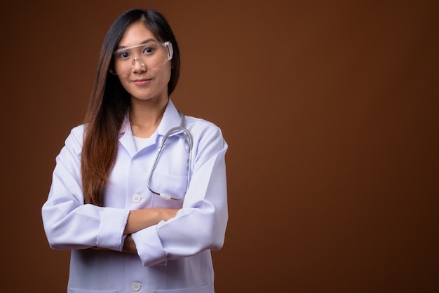 Young beautiful Asian woman doctor wearing protective glasses ag