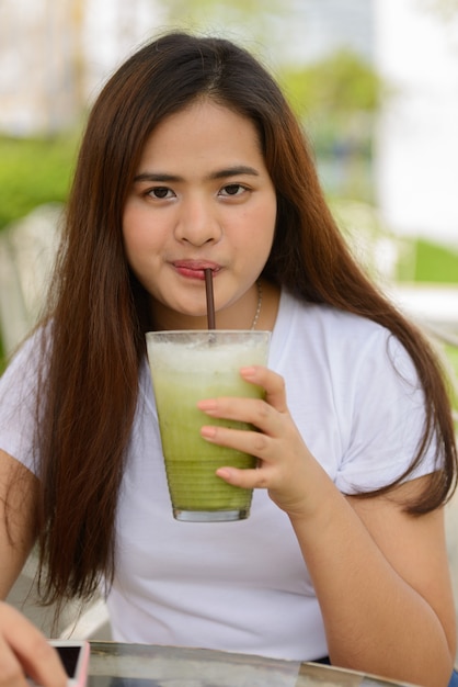 屋外のコーヒーショップでアイスグリーンティーを飲む若い美しいアジアの女性