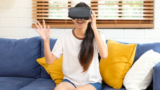 Young beautiful asian woman exciting in VR headset looking up and trying to touch objects in virtual reality at home living room