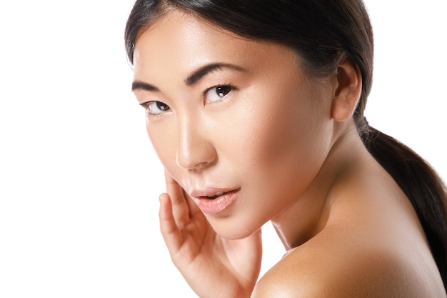 Young and beautiful asian woman is posing in studio on white wall