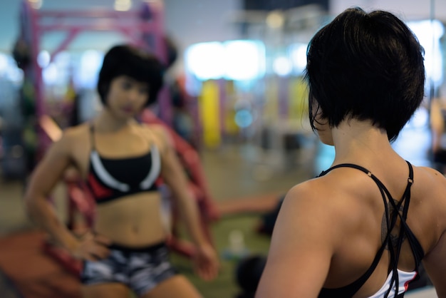 Young beautiful Asian woman looking at mirror in gym