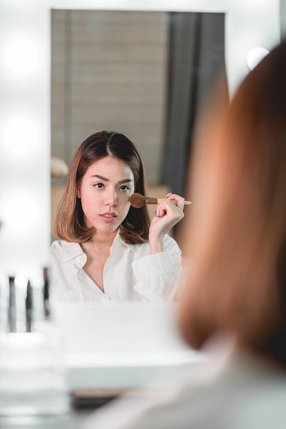 Giovane bella donna asiatica che fa trucco vicino allo specchio