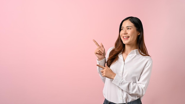 Young beautiful Asian woman pointing finger to the side on pink isolated background