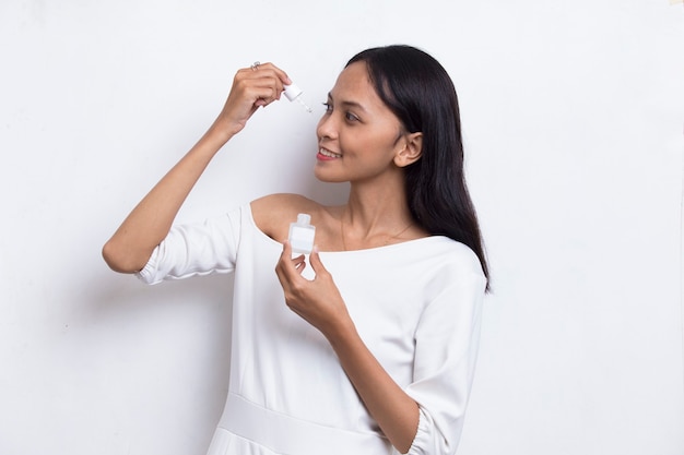 Young beautiful asian woman putting moisturizing serum to her face isolated on white background