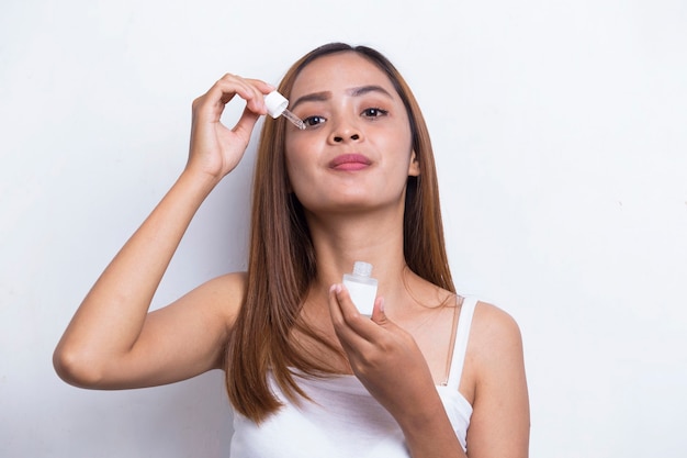 young beautiful asian woman putting moisturizing serum to her face isolated on white background