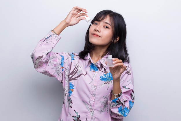 young beautiful asian woman putting moisturizing serum to her face isolated on white background