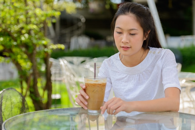 屋外のコーヒーショップに座っている若い美しいアジアの女性