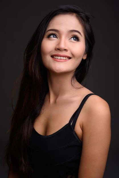 Young beautiful Asian woman smiling against gray