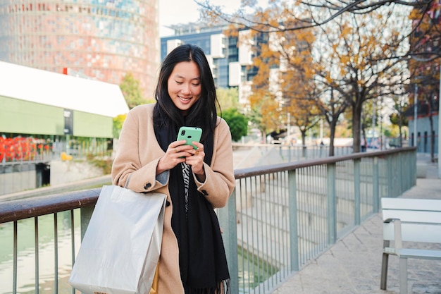 若い美しいアジア人女性が笑顔でスマートフォンアプリで メッセージを入力しています 幸せな中国人の肖像画です