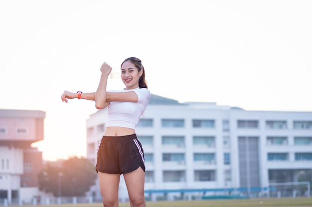 A young beautiful Asian woman in sports outfits doing stretching before workout outdoor in the park in the morning to get a healthy lifestyle. Healthy young woman warming up outdoors