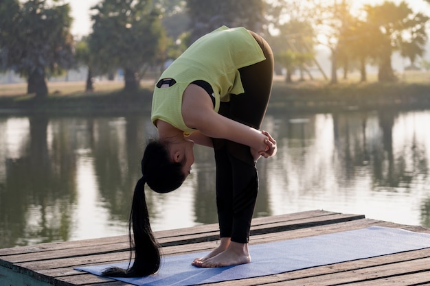 Young beautiful Asian woman in sports outfits doing yoga outdoor in the park in the morning with warm sunlight for a healthy lifestyle. Young woman yogi doing yoga in morning park