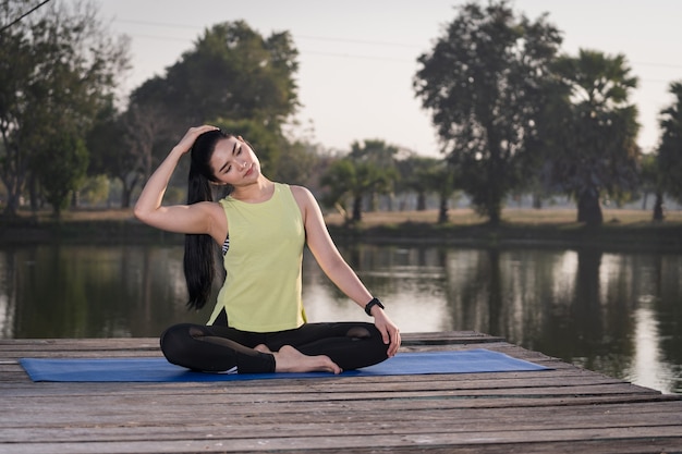 Giovane bella donna asiatica in abiti sportivi che fa yoga all'aperto nel parco al mattino con una calda luce solare per uno stile di vita sano. yogi di giovane donna che fa yoga nel parco mattutino
