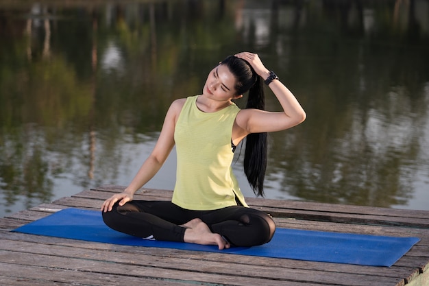 Giovane bella donna asiatica in abiti sportivi che fa yoga all'aperto nel parco al mattino con una calda luce solare per uno stile di vita sano. yogi di giovane donna che fa yoga nel parco mattutino