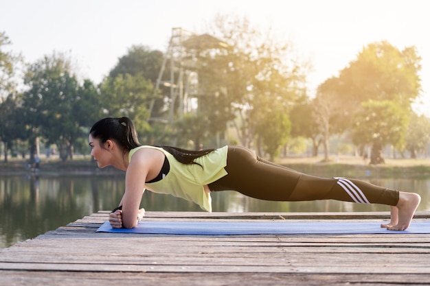 스포츠 복장을 한 젊은 아시아 여성이 아침에 공원에 판자를 깔고 균형과 힘을 연습하여 건강한 생활 방식을 취합니다. 판자 운동을 하 고 젊은 아름 다운 운동 여자.