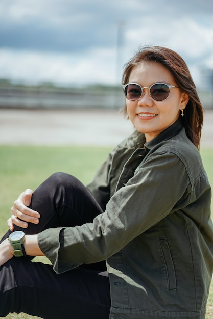 Young Beautiful Asian Woman Wearing Jacket And Black Jeans Posing Outdoors Sitting on the park