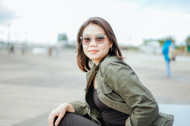 Молодая красивая азиатская женщина в куртке и черных джинсах позирует на открытом воздухе