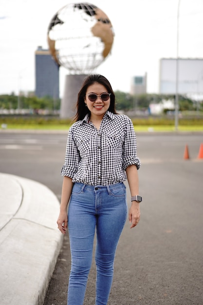 Молодая красивая азиатская женщина в клетчатой рубашке и синих джинсах позирует на открытом воздухе