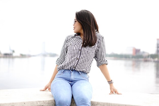 Young Beautiful Asian Woman Wearing Plaid Shirt And Blue Jeans Posing Outdoors