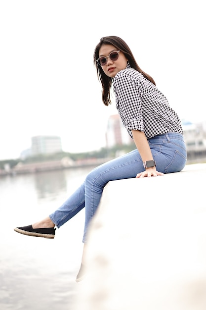 Young Beautiful Asian Woman Wearing Plaid Shirt And Blue Jeans Posing Outdoors