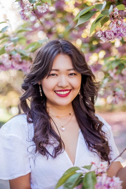 A young beautiful Asian woman in a white dress walks in a flowered park