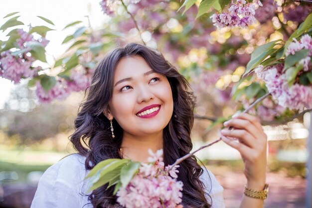 A young beautiful Asian woman in a white dress walks in a flowered park