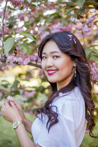 A young beautiful Asian woman in a white dress walks in a flowered park