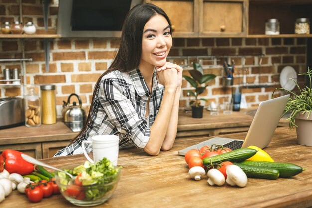 Young beautiful asian woman with laptop on kitchen finding recipes and smiling. Close-up.