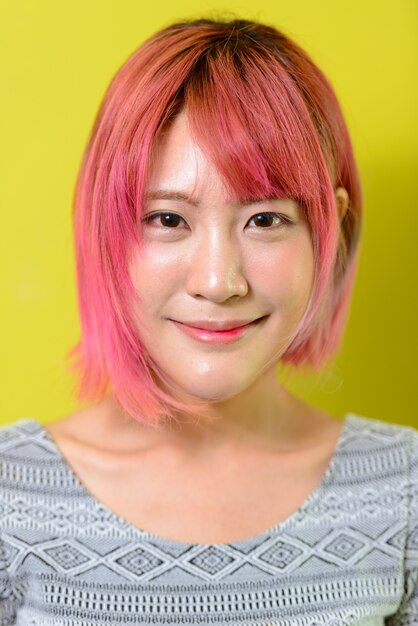  young beautiful Asian woman with pink hair against yellow wall