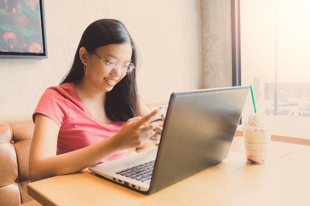 Young beautiful asian woman working with laptop in coffee shop background with vintage filter