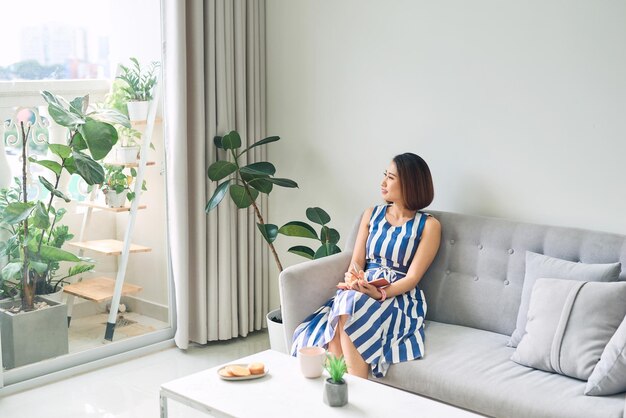 Photo young beautiful asian woman writing and sitting on sofa in living room