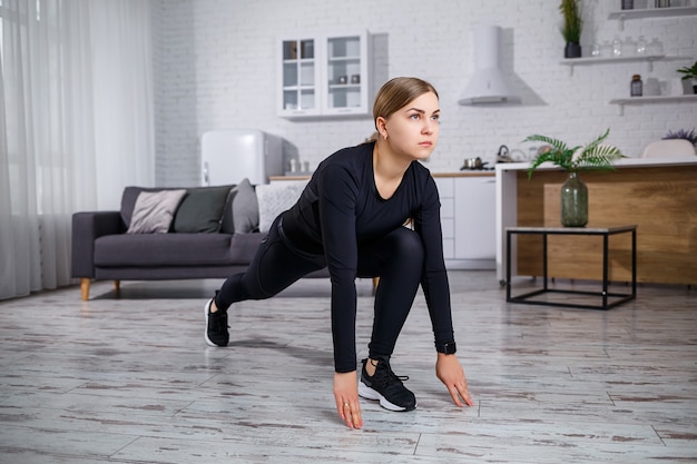 Young beautiful athletic woman in black leggings and top doing warm-up exercises at home. Healthy lifestyle. Girl in fitness clothes. The woman goes in for sports at home.