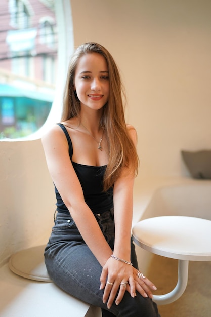 Young beautiful and attractive woman with long brown hair in a black dress at cafe against urban background.