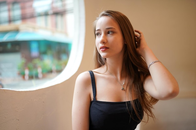 Young beautiful and attractive woman with long brown hair in a black dress at cafe against urban background.