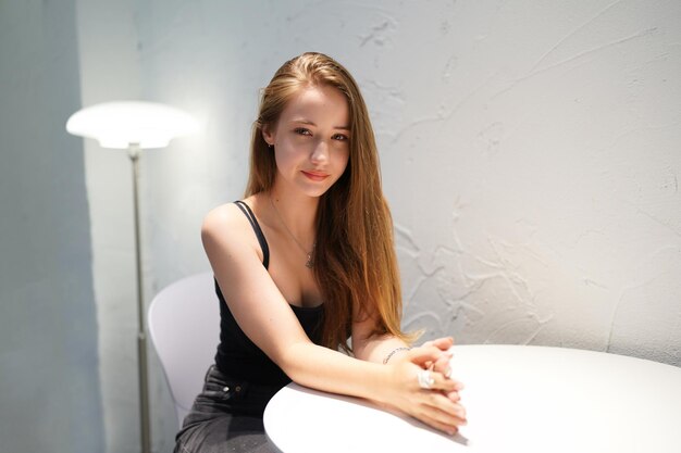 Young beautiful and attractive woman with long brown hair in a black dress at cafe against urban background.