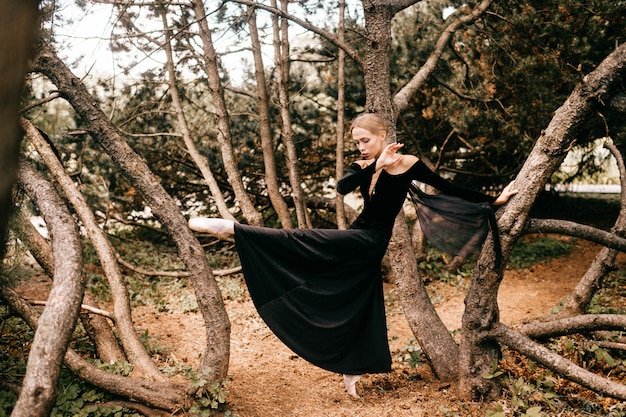 Giovane bella ballerina in abito vintage nero con velo in posa tra gli alberi