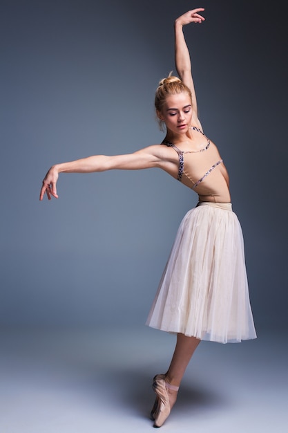 Молодая красивая балерина танцует на студийном сером фоне