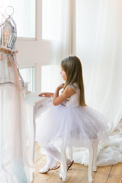 young beautiful ballet ballerina sits on an ottoman in front of a mirror. Little girl