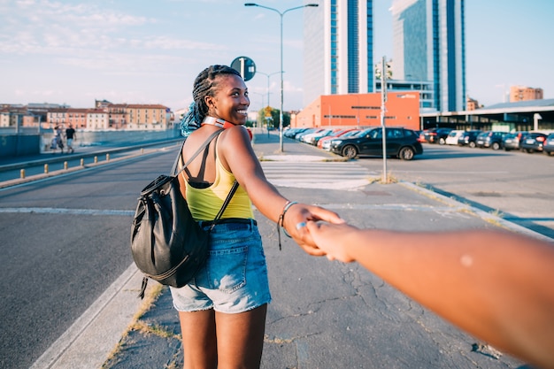 Young beautiful black woman outdoor holding hand walking on the road, smiling