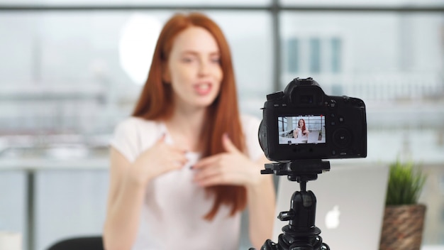 Young beautiful blogger girl working in office while shooting on camera